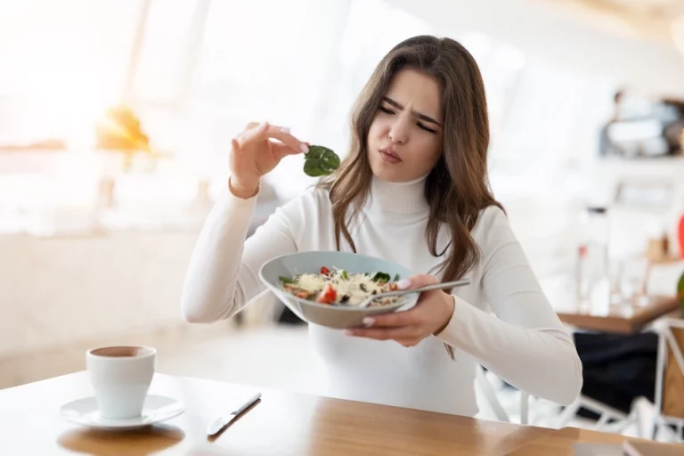 cliente mécontante et faisant la moue en brandissant une pousse d'épinard qui vient de son assiette de salade.