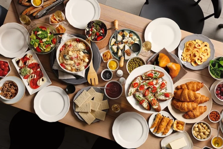 C'est une table dressée pour 5 personnes et garnie de plats sucrés et salés à partager tous alléchants ; tomate-mozza, salade verte, salade de fruits, brochette, croissant, salade l'épinard, plateau de fromage, fruit, noix, ...